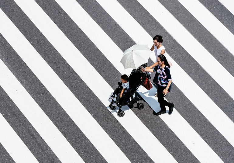 picture of two woman and a baby in a stroller pram crossing a street 