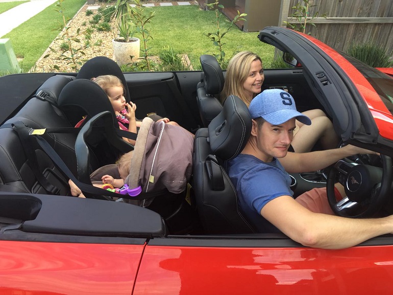 picture of a woman and a men driving in a car with kids in different car seats on the back