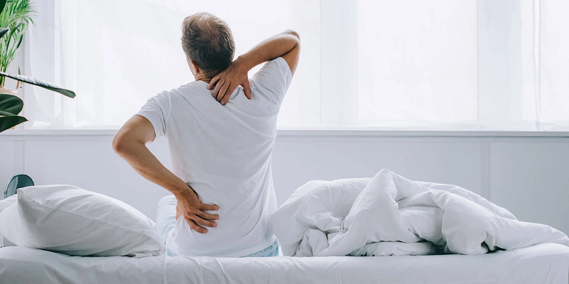 man experiencing back pain and sitting down on memory foam mattress